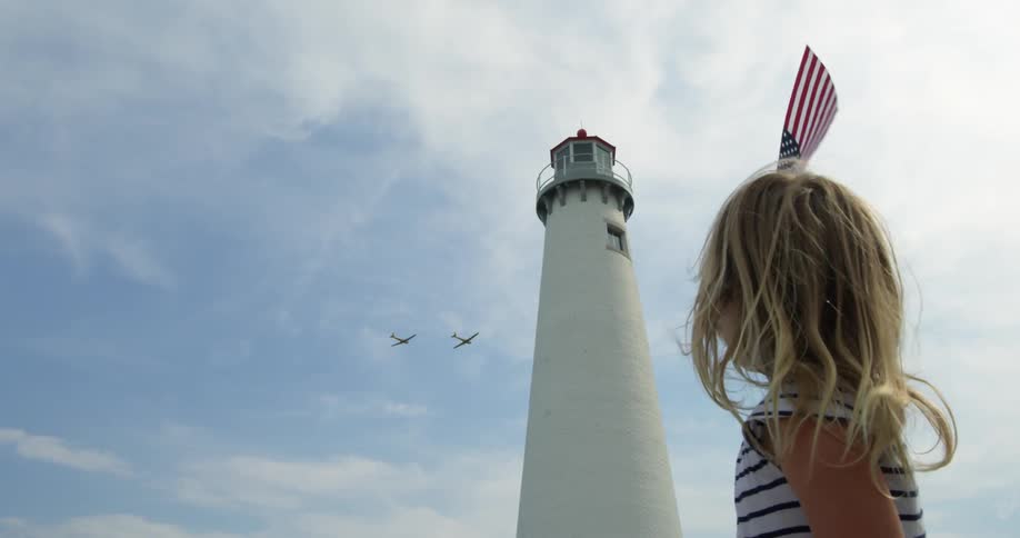 A child waves a flag before a lighthouse as planes fly in the air