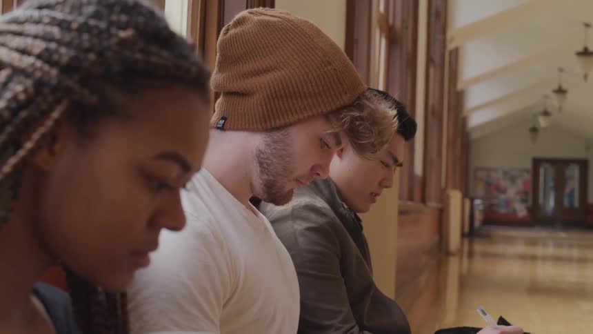 Three college students sit on a bench and work on homework between classes