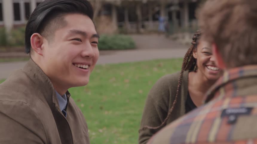 Two men and a woman smiling and talking with grass and buildings in the background