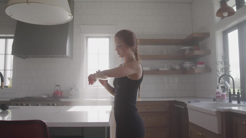 Woman with a ponytail uses a smartwatch in kitchen