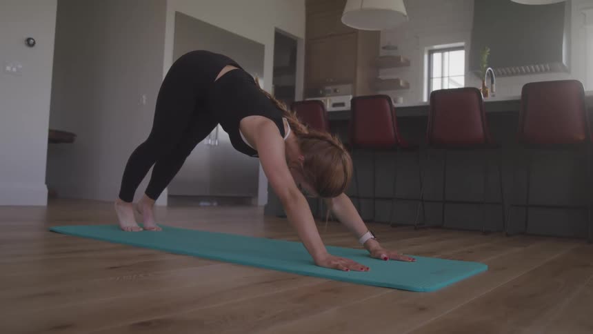 A woman leans down and stretches backward in a yoga pose in her kitchen