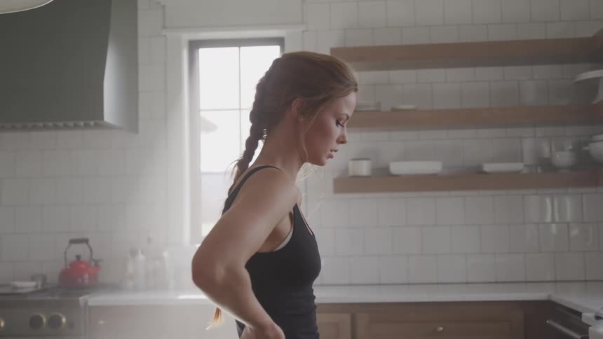 A young woman in fitness apparel stands in the middle of a kitchen