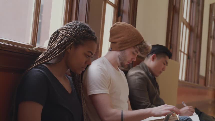 Students sit on bench in long wide hall studying
