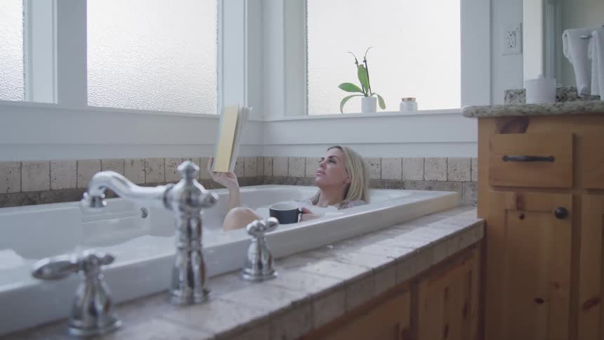 A woman is reading a book while relaxing in a bath tub