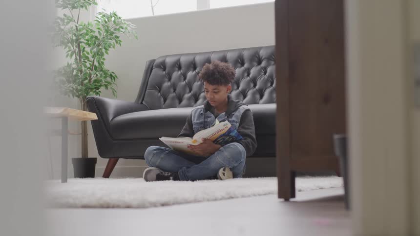 A young boy sitting on the floor in front of a couch reads a book