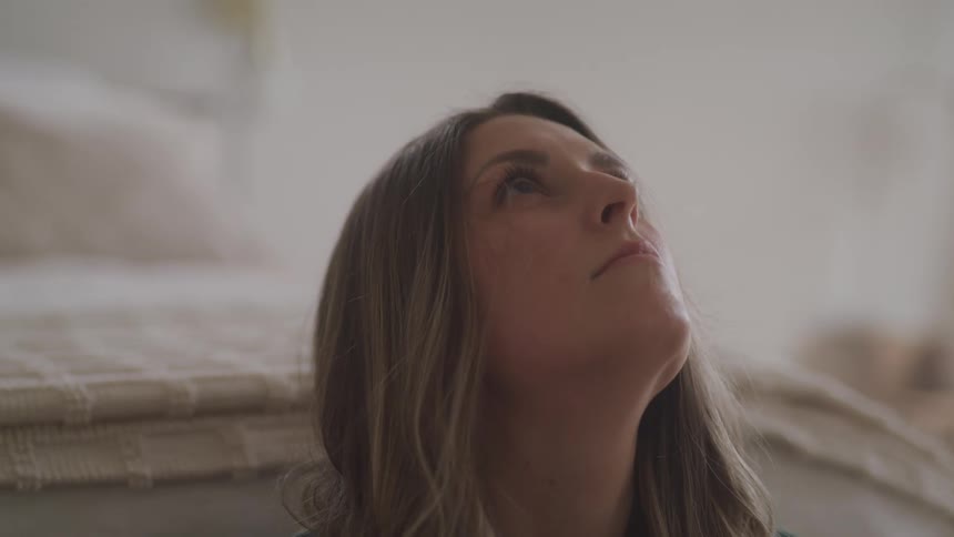Woman sitting in the floor of a bedroom looks up while reclined on the bed