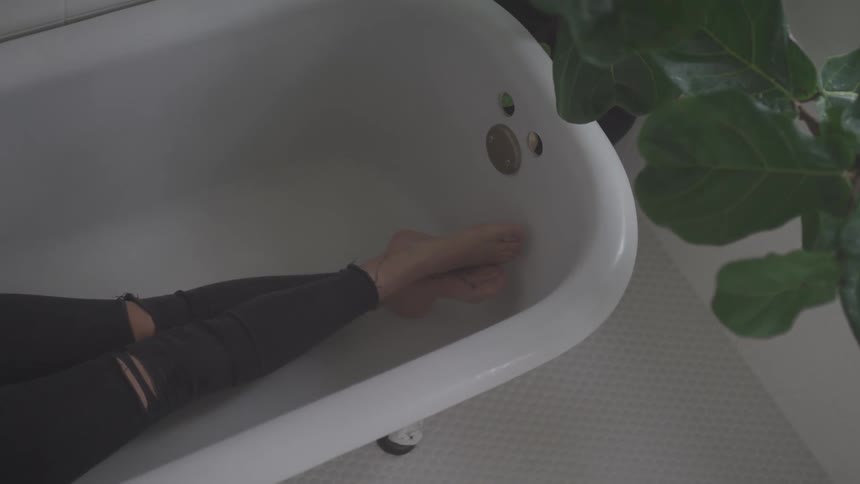 Woman with ripped jeans lies in a bathtub in the bathroom