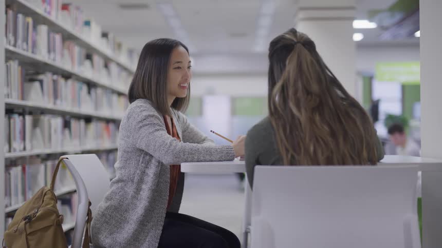 Students sit in library conversing as they work