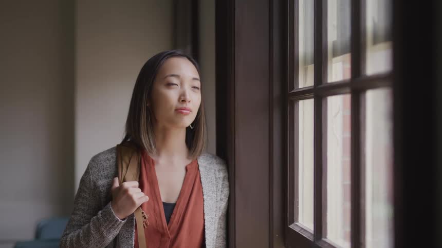 A woman is standing indoors and looking out the window