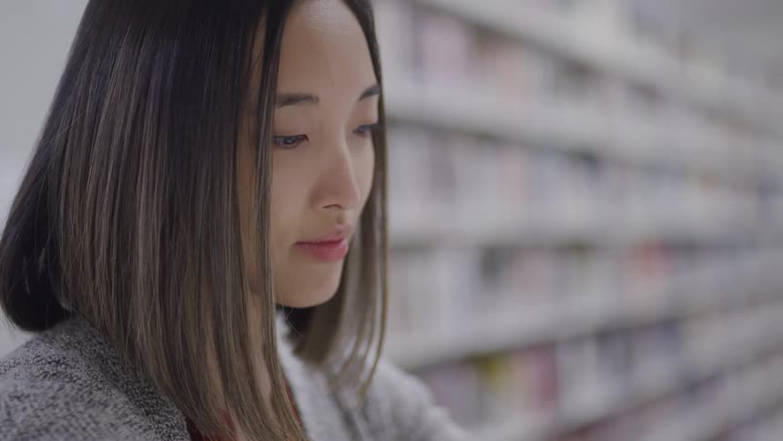 A woman with a sweater looking downward with shelves in the background