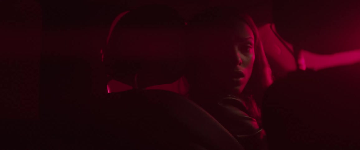 A woman sits in a car at night and looks into the backseat