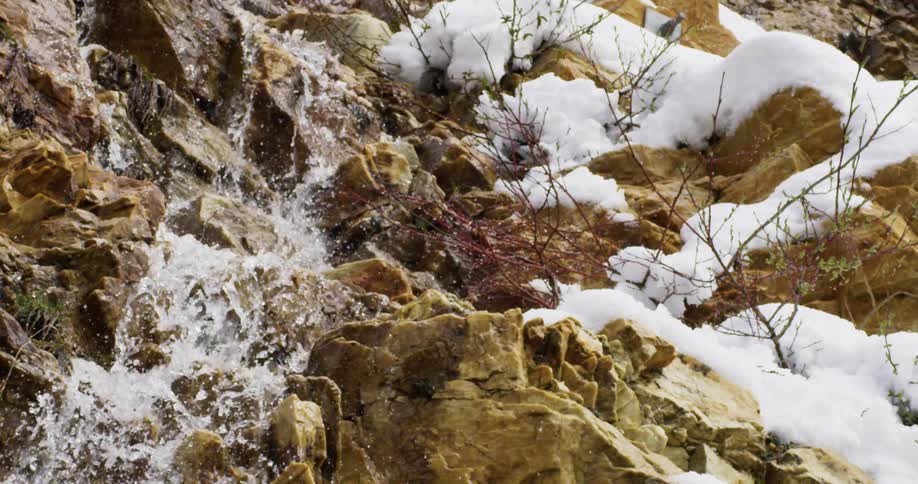 A stream of water falls down a rocky cliff face covered in snow