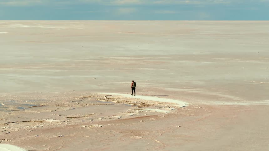 Aerial rise as a woman hikes through a vast barren desert on a sunny day