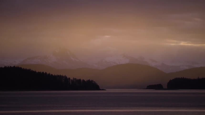 A lake with snow capped mountains in the background is seen at dawn