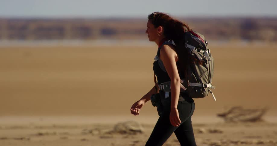 A woman with a backpack and a camera walking through a hot desert land