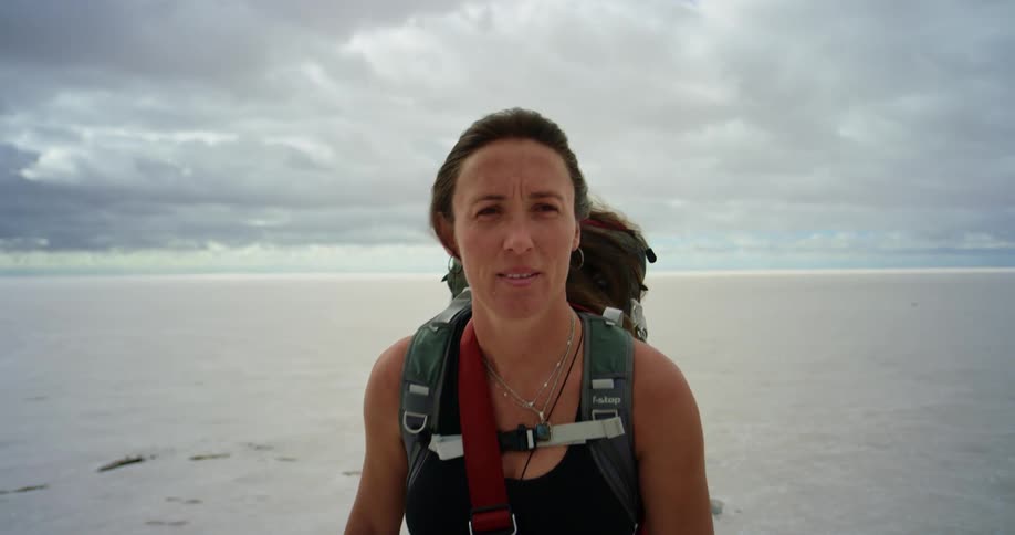 A female hiker wearing a backpack hikes through a desert as thick clouds loom overhead