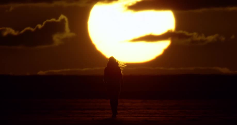 Woman walks towards the huge setting sun