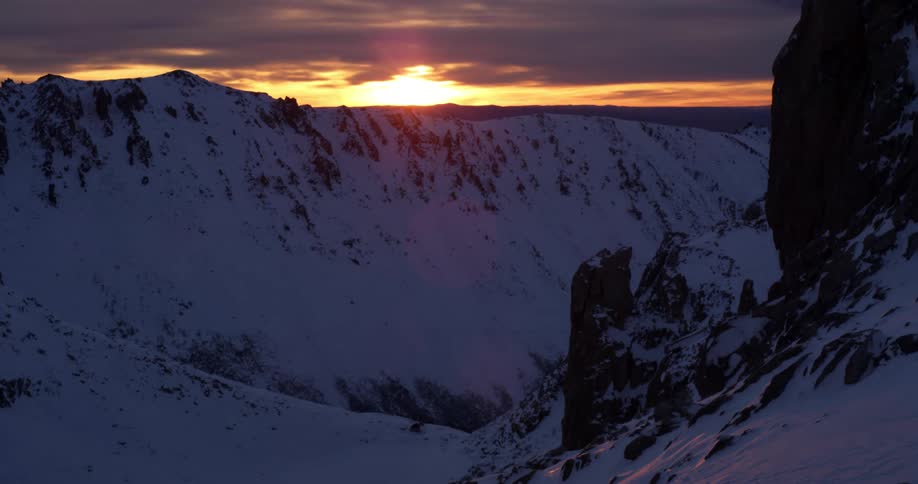 The sun sets behind the snow covered mountains