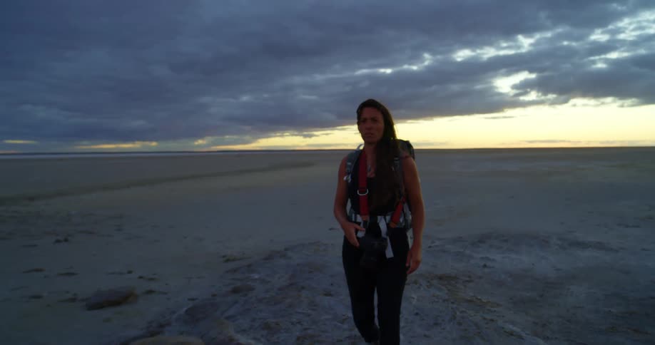 A woman walks through a moody desert and takes a photo