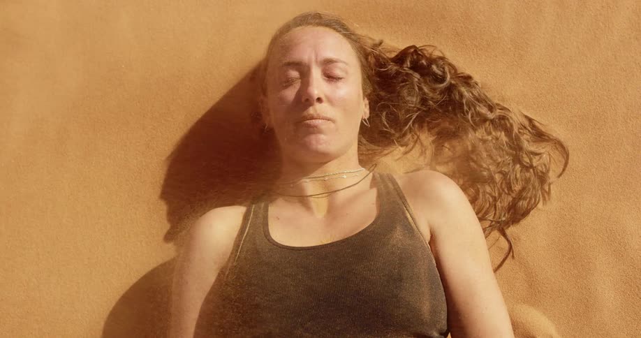 A woman lays still in blowing sand