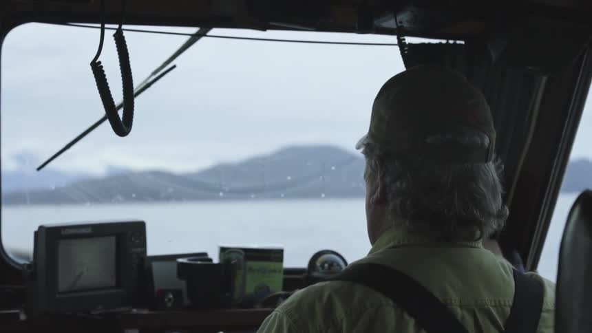 A man pilots a boat on a lake on a cloudy day
