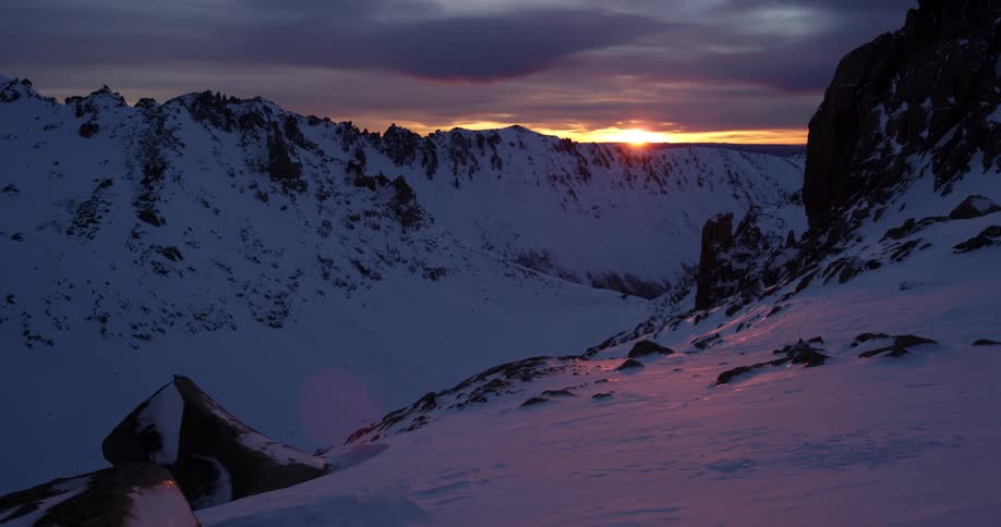 Pan over snowy mountains in the setting sun