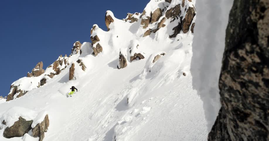 A skier descends a steep and rocky slope on a sunny day