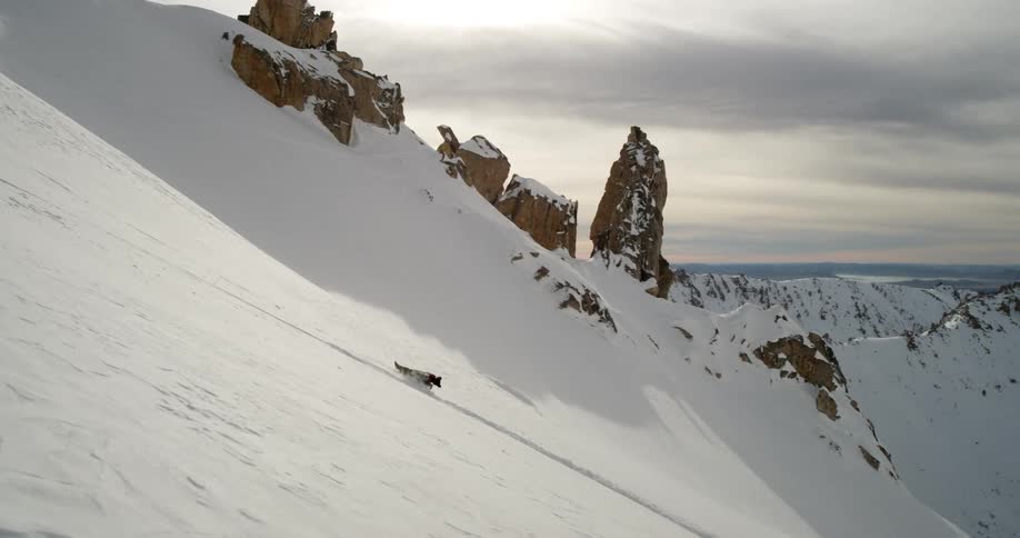 Black dog runs downhill through snowy mountains