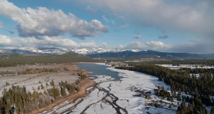 An aerial view of a river with snow and a forest