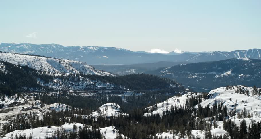 Hills and forest border a river in a wintery landscape below a mountain ridge on a sunny day