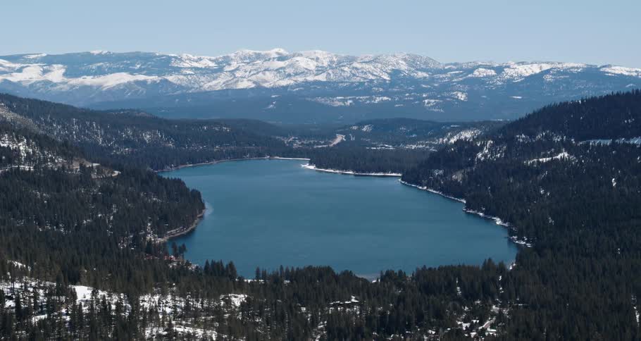 An aerial view of a lake near a forest and mountains is displayed