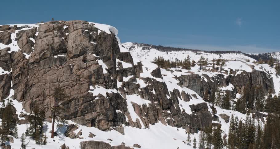 An aerial view of snowy mountains with pine trees on a winter day