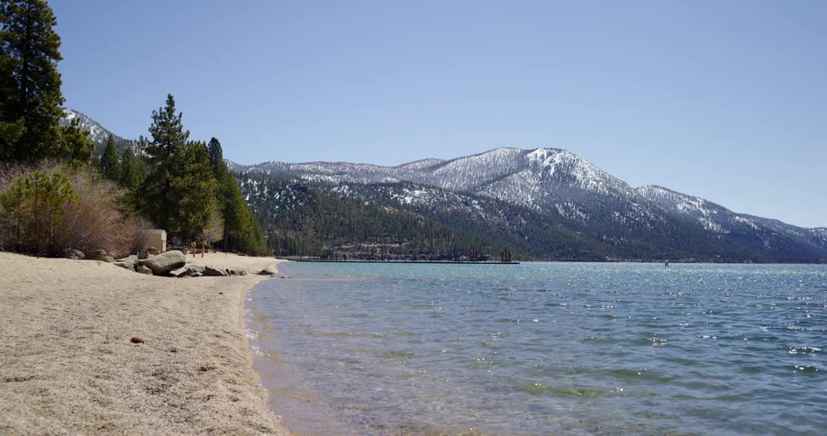 The beach of a lake beneath a snowy mountain on a sunny day
