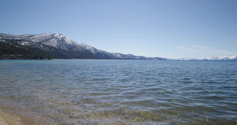 Water splashes onto the shore of a beach near a snow topped mountain