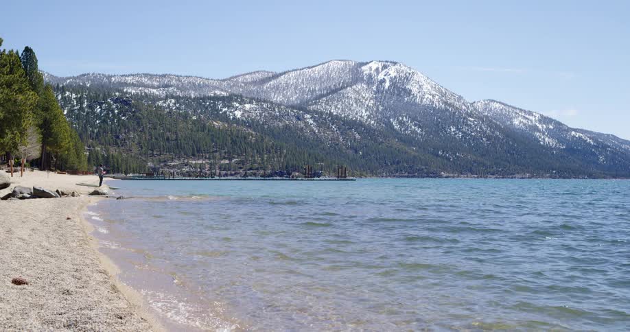 A man standing on the shore with hills in the background