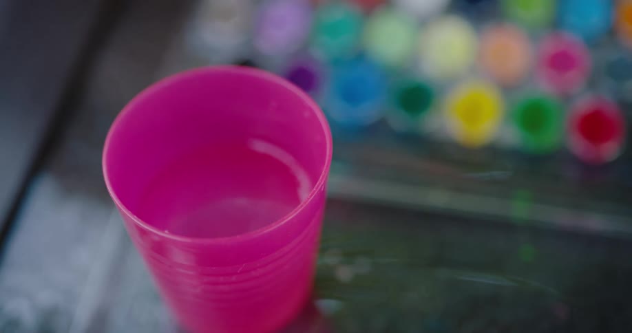 A painter wets a brush in a cup of water to use watercolor paints