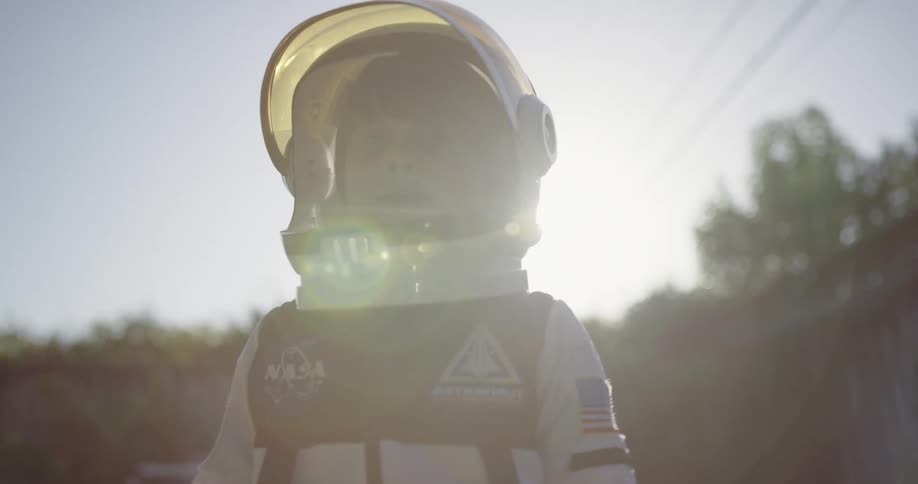 Young boy wearing an astronaut suit with helmet plays in the backyard at sunset