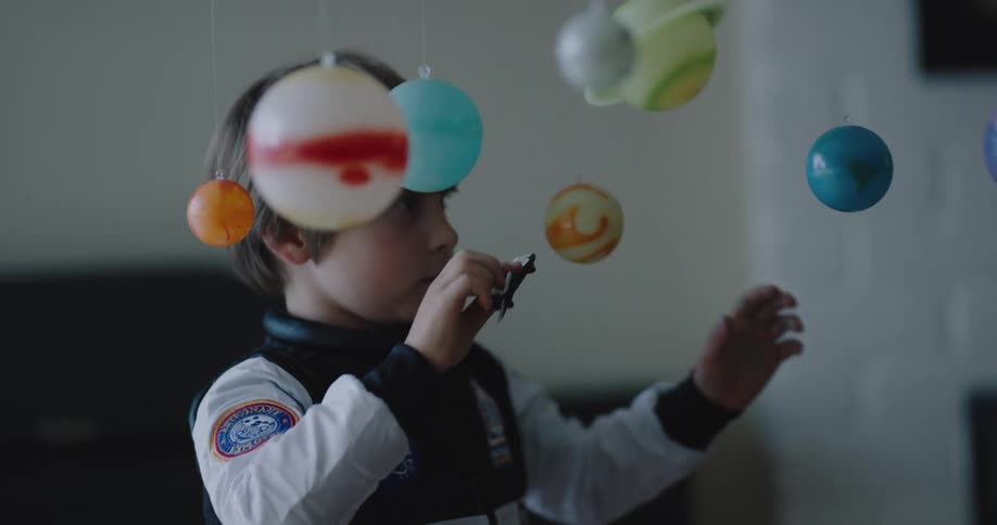A boy with a nasa costume is playing with a ship