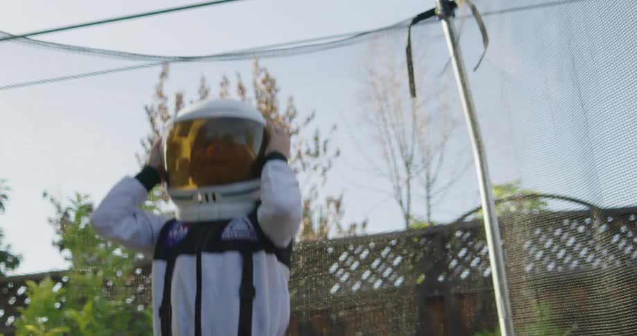 A young boy dressed in an astronaut costume bounces up and down on an outdoor trampoline