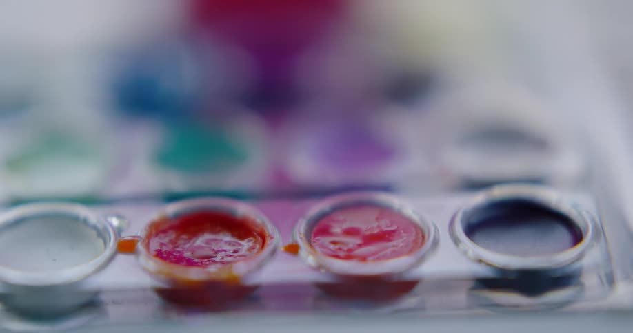 A person dipping a paint brush into water color paints