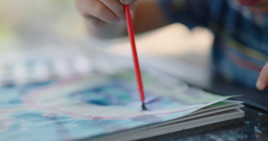 A young boy paints with watercolors on a sheet of paper while sitting at a table