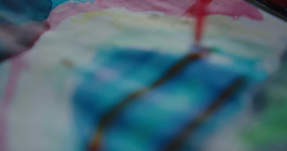 A person dips a paint brush in paint and paints on a piece of paper