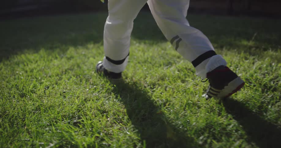 Male child wearing an astronauts suit carefully walks through the grass in a fenced in backyard as he pretends to be walking in space