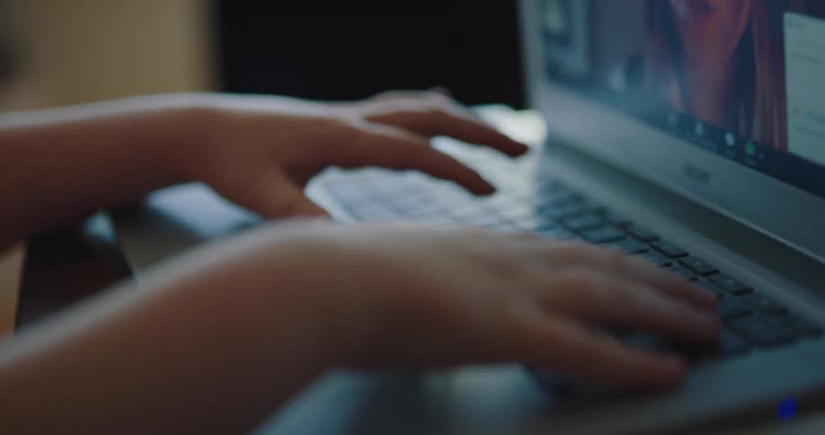 A child types on a laptop while video chatting with a woman displayed on the screen
