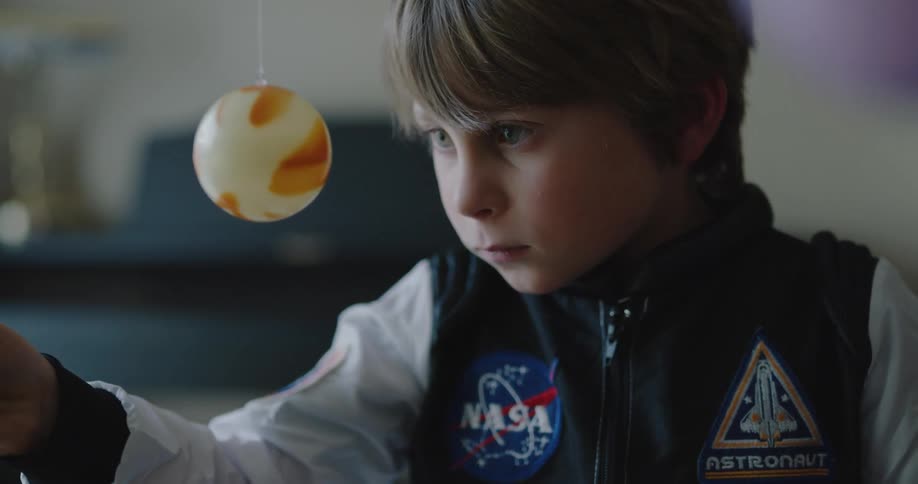 A little boy plays with a toy spaceship and planets in his house