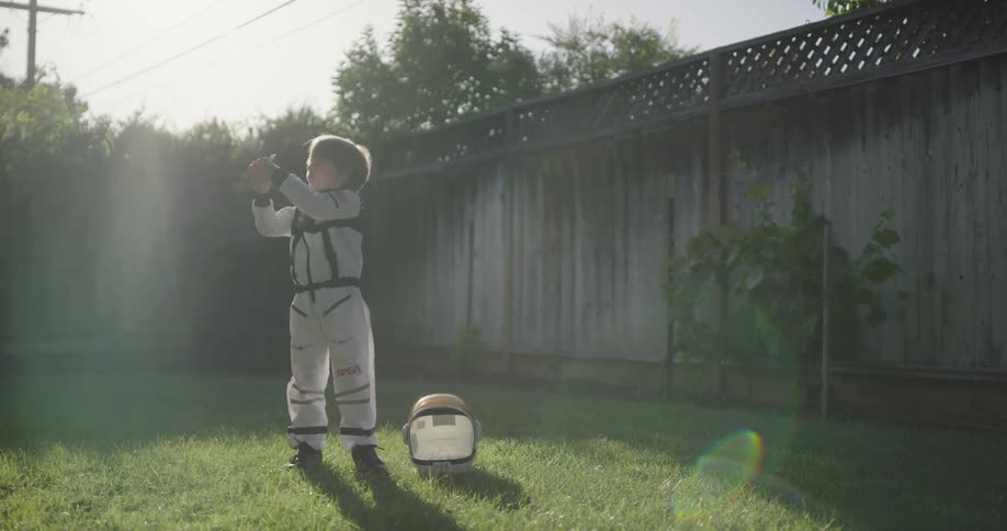 A little boy in an astronaut costume plays in his backyard