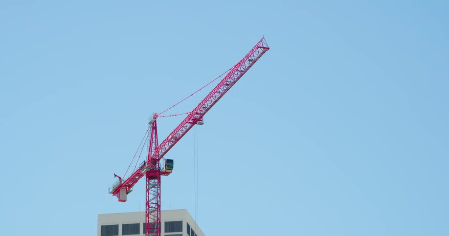 Red construction crane contrasts with clear blue sky as it towers over building