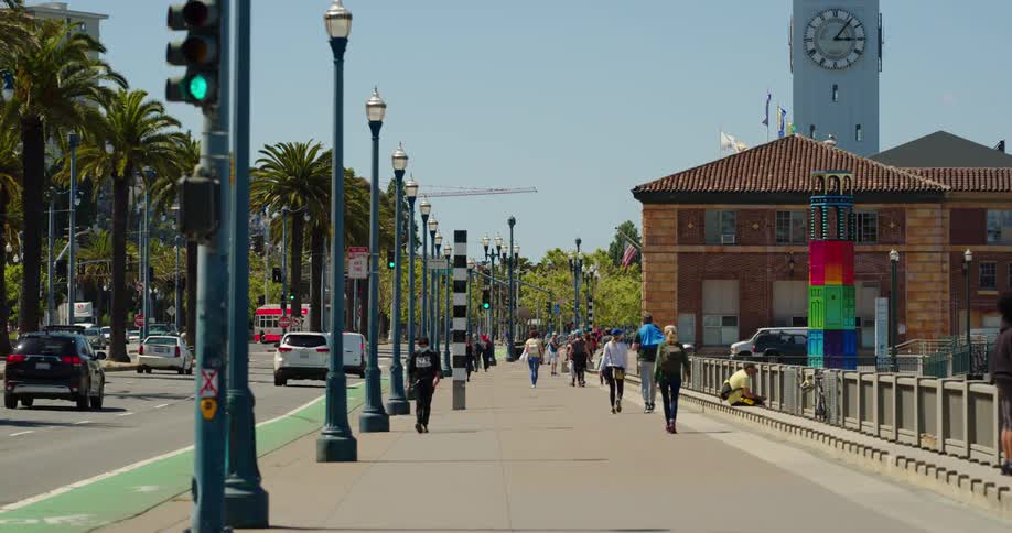 People walk down a city sidewalk as cars drive down the street