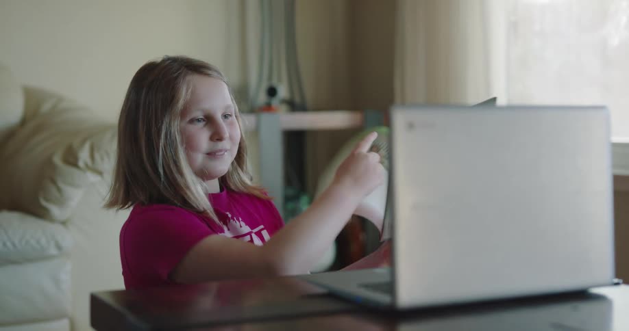 A young girl at home uses a laptop computer to show her school work during online class
