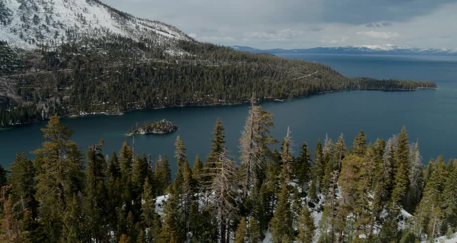 A large coastal bay is lined by evergreen forests and snowy mountains